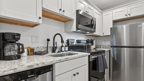 A modern kitchen with white cabinets, stainless steel appliances, a coffee maker, and a dishwasher. - St. Johns Nest, Near Cathedral Park (Portland)