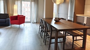 Ein modernes Wohnzimmer mit Essbereich, ausgestattet mit einem Holztisch, einem roten Sessel und einem großen Fenster mit Vorhängen.