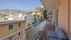 Un balcón con sofá y mesa, con vistas a una zona residencial con edificios y una montaña al fondo.
