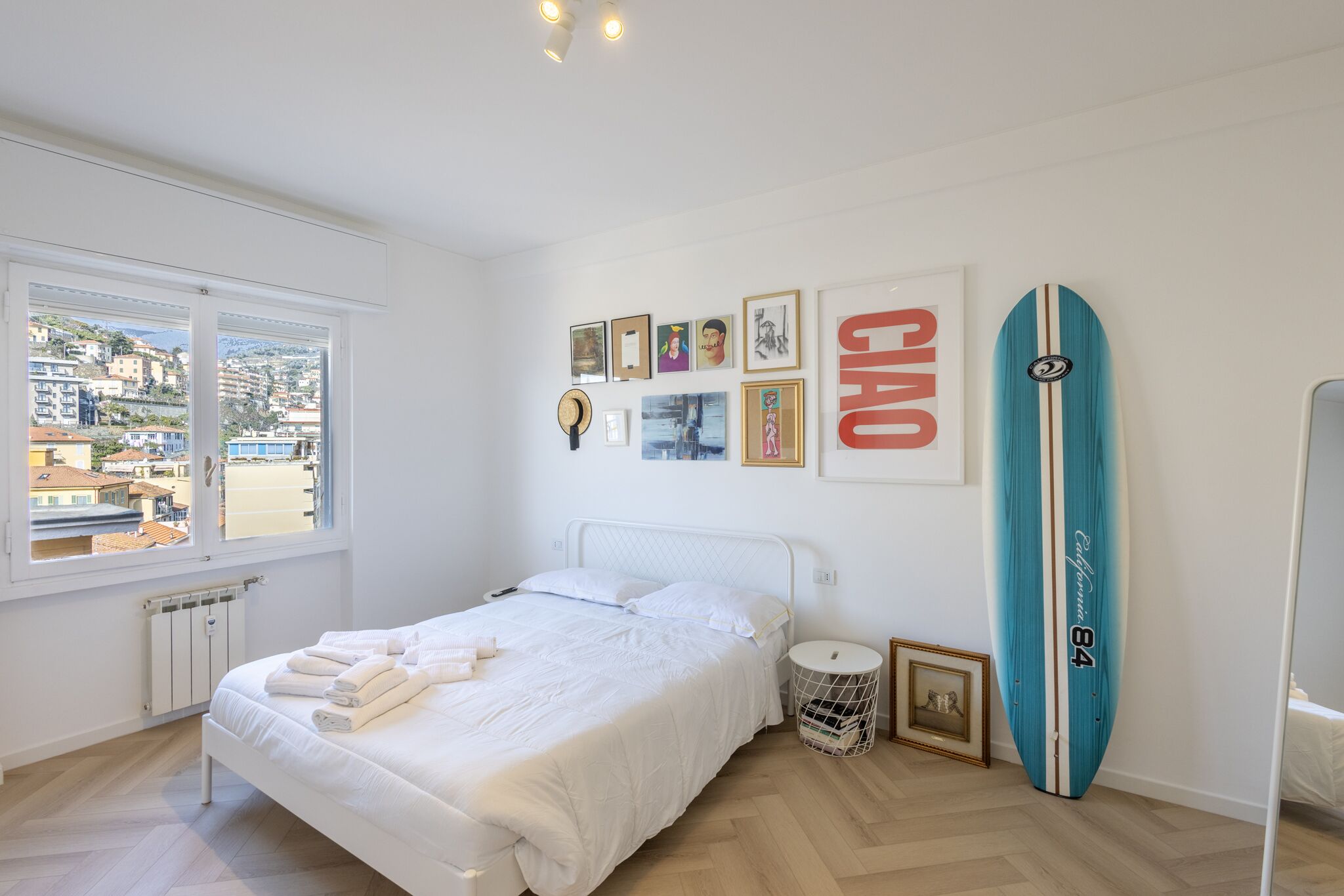 Un dormitorio con cama, ventana con vistas, una tabla de surf y cuadros en la pared.