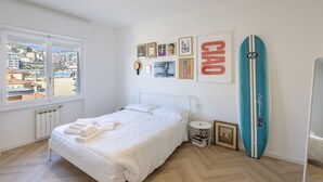 Un dormitorio con cama, ventana con vistas, una tabla de surf y cuadros en la pared.