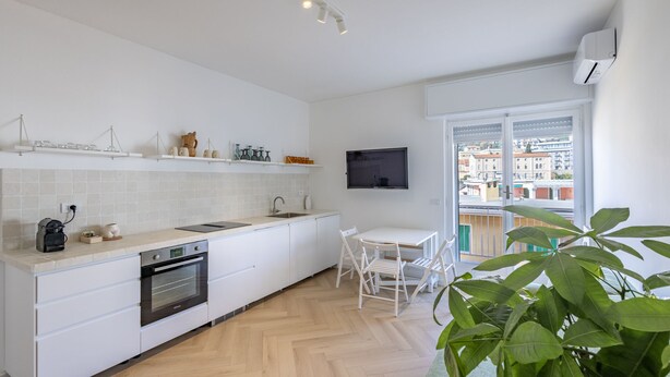 Una cocina moderna con armarios blancos, horno empotrado y comedor con mesa y sillas blancas.
