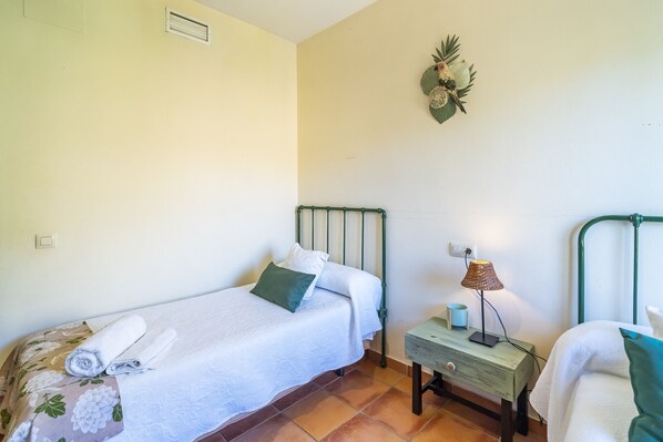 A small, clean room with two beds, a nightstand, a lamp, and a wall decoration.
