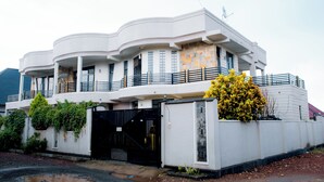 A modern multi-story building with a curved facade, balconies, and a gated entrance. - THE MOON APARTMENTS (Gisenyi)