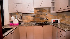 A kitchen with beige cabinets, a granite countertop, a microwave, and a gas stove. - THE MOON APARTMENTS (Gisenyi)