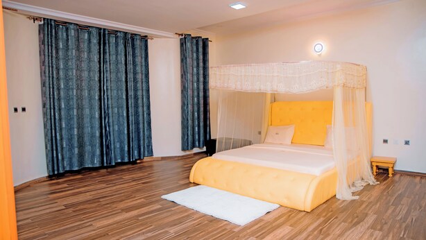 A bedroom with a bed, curtains, a bedside table, and a nightstand. - THE MOON APARTMENTS (Gisenyi)
