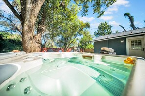 A hot tub in a backyard with a tree and a barbecue grill.
