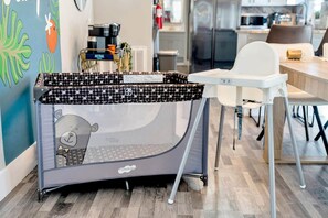 A baby playpen with a bear design, a white chair, and a kitchen area in the background.