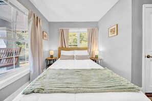 A bedroom with a bed, two bedside tables, a window with curtains, and a door.