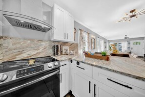 A modern kitchen with white cabinets, a stainless steel stove, and a marble countertop.