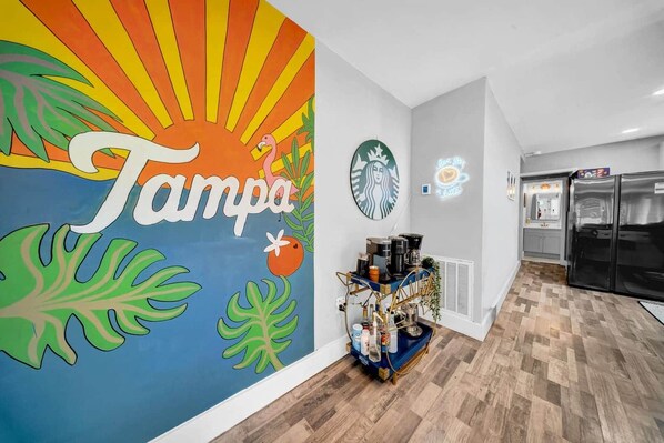 A modern kitchen with a vibrant wall mural, a coffee station, and a large refrigerator.