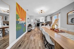 A modern kitchen with white cabinets, a wooden dining table, and a colorful wall mural.