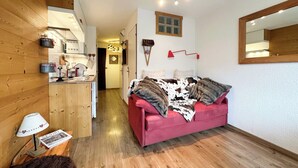 Un salon chaleureux avec un canapé rouge, un plancher en bois et un coin cuisine équipé d’appareils électroménagers modernes.