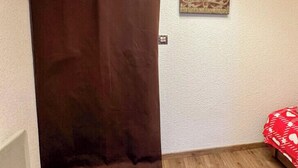 Une pièce avec un plancher en bois, un rideau marron, un luminaire fixé au mur et un tableau encadré.