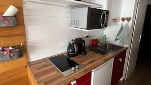 Une cuisine compacte équipée d’un micro-ondes, d’une bouilloire et d’un grille-pain sur le plan de travail, d’un petit évier et d’armoires en bois.