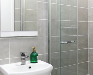 Een badkamer met een witte wastafel, een spiegel en een douchecabine met glazen wanden.