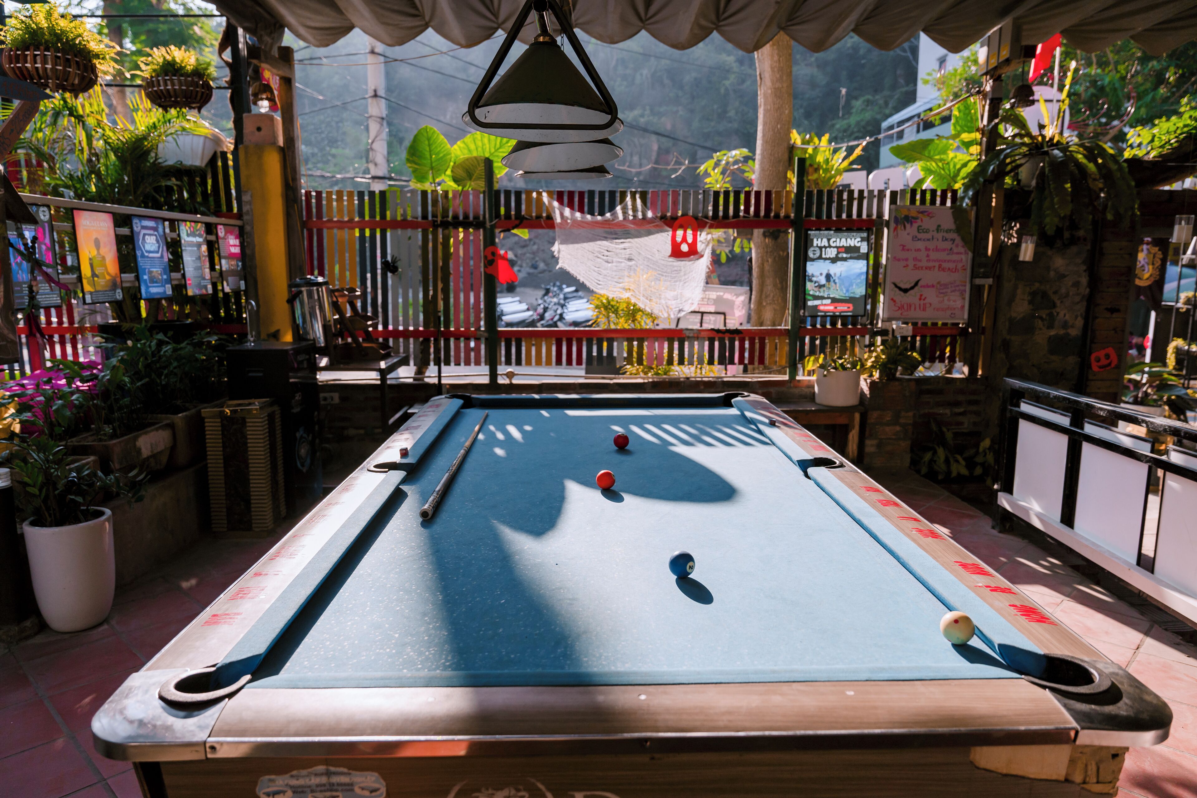 A pool table in a room with a view of a street and greenery outside.