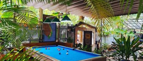 An indoor pool area with a blue pool, surrounded by lush greenery and a covered seating area.