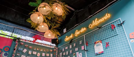 A room with a teal wall, a neon sign reading "Secret Garden Moments", and a grid of photos on the wall.