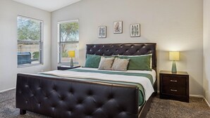 Ein Schlafzimmer mit einem dunkelbraunen Leddbett, einem Nachttisch mit Lampe und drei an der Wand befestigten Kunstwerken.