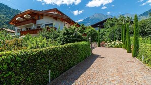 A building with a balcony, a cobblestone path, and a mountainous backdrop.