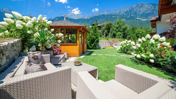 A patio with wicker furniture, a wooden gazebo, and a well-maintained lawn with flowers.