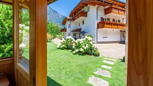 A wooden-framed room with a view of a white building with balconies and a garden with white flowers.