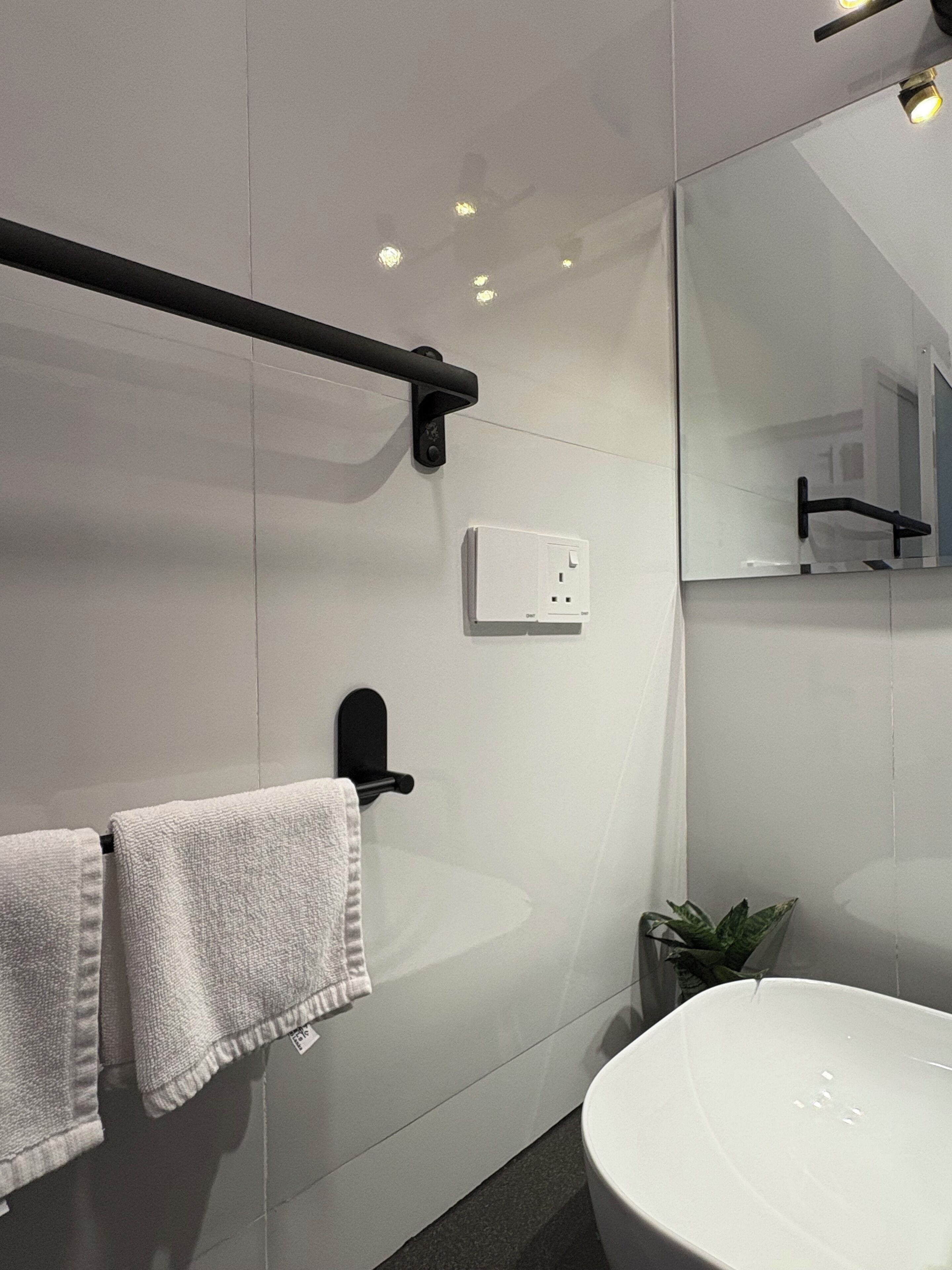 A modern bathroom with a large mirror, a towel rack, a sink, and a small plant.