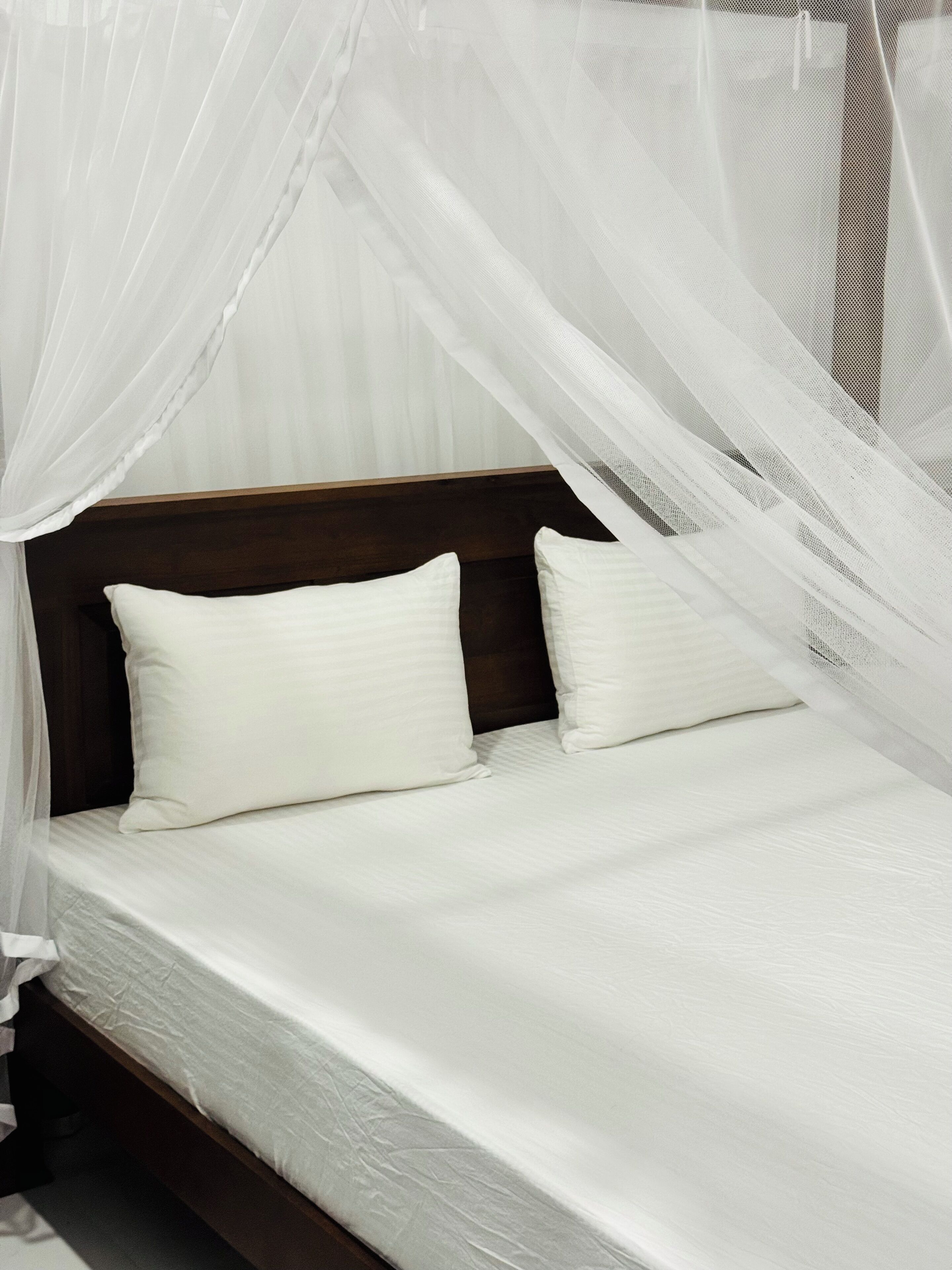 A bed with white bedding and a wooden headboard, under a white canopy.