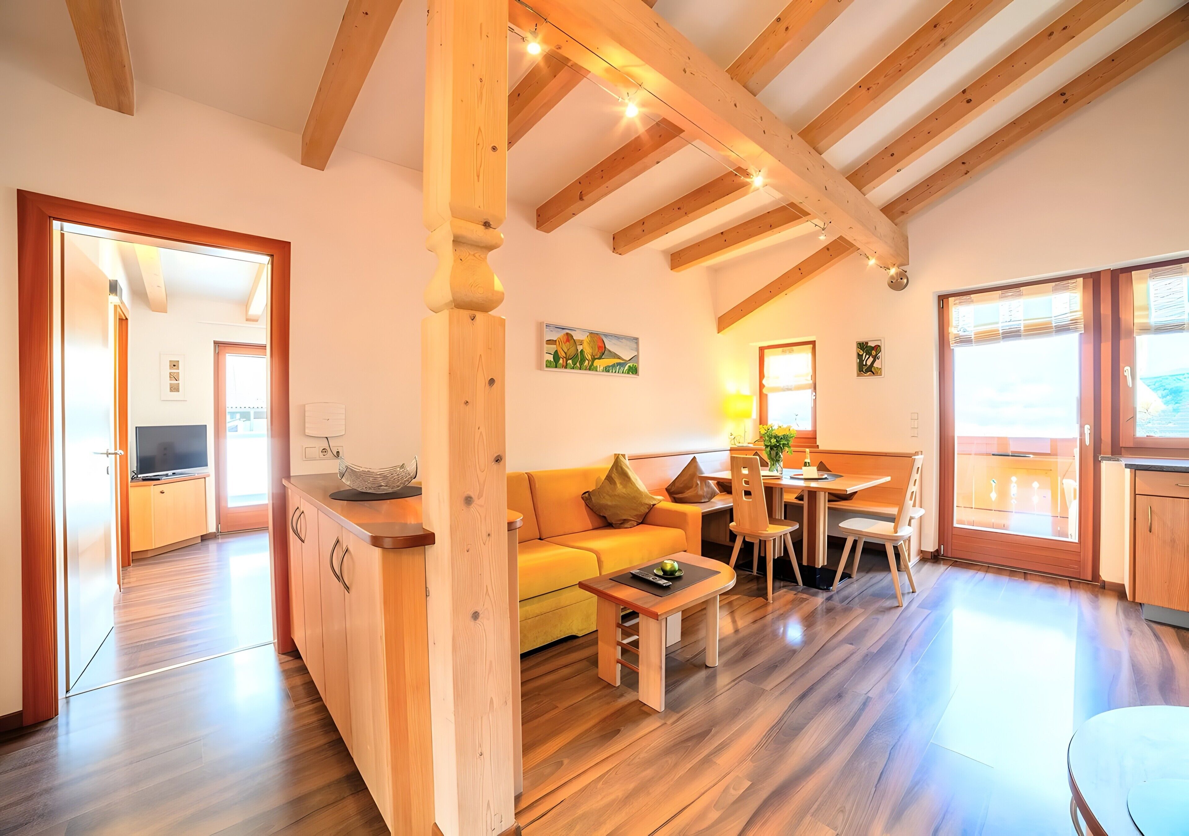 Una sala de estar moderna con vigas de madera, un sofá, una mesa de centro y un comedor con sillas y una mesa.