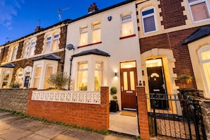 A row of terraced houses with a brick facade, white window frames, and a gated entrance. - Cardiff 4-Bed House | Hot Tub, Games Room & Private Garden (Cardiff)