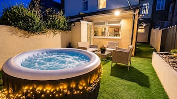 Een buitenzwembad met verlichting, omringd door een terras met stoelen en een tafel.