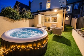 An outdoor hot tub with lights, surrounded by a patio area with chairs and a table. - Cardiff 4-Bed House | Hot Tub, Games Room & Private Garden (Cardiff)