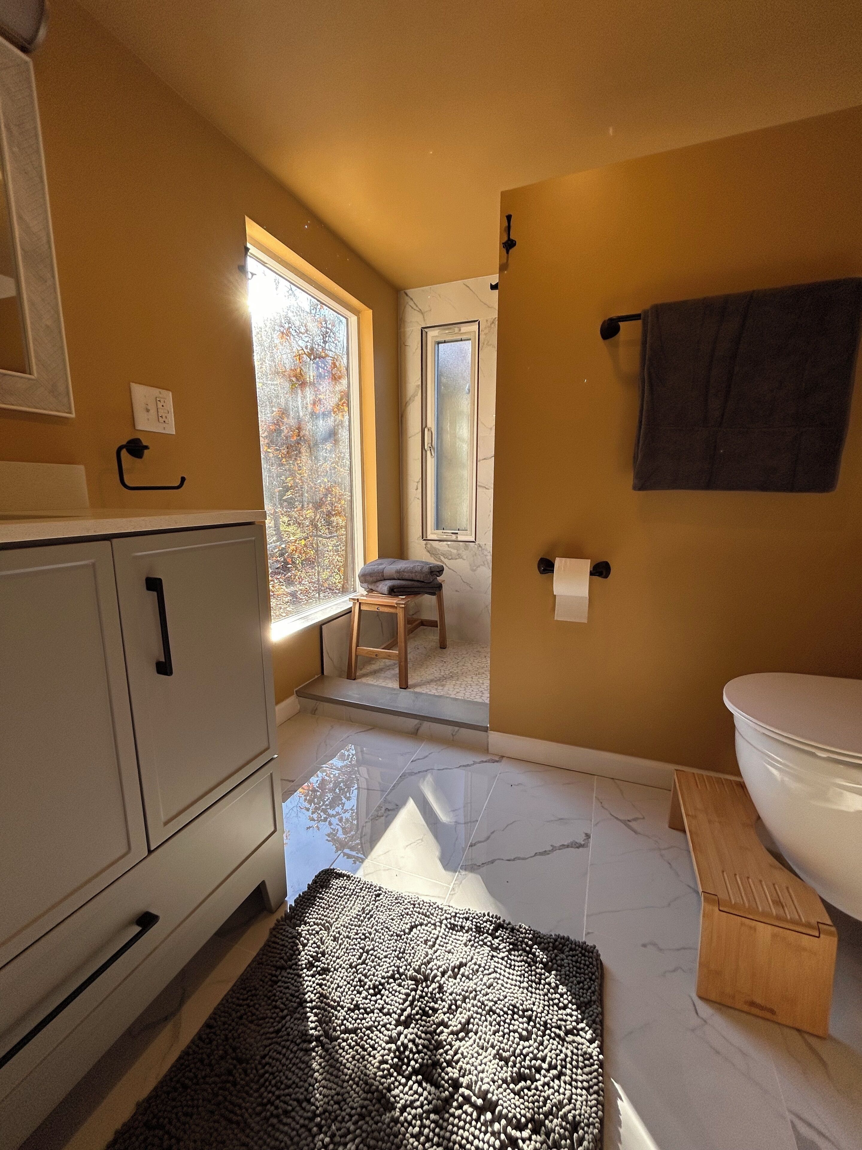 Een badkamer met toilet, wastafel en spiegel. Er is een raam dat voor daglicht zorgt, en een handdoekrek is zichtbaar.