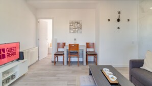 Ett modernt vardagsrum med en matplats, en tv-skärm som visar texten ”KLAR FÖR GÄSTER” och en väggklocka.
