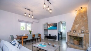 Een moderne woonkamer met een bank, salontafel, eethoek en een stenen openhaard.