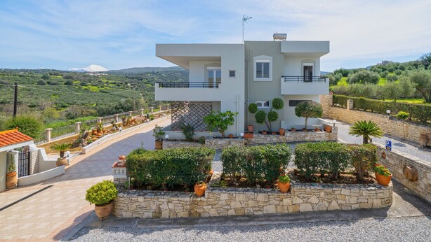 A modern two-story house with a stone facade, a balcony, and a landscaped garden with potted plants. - Villa Pantelis with private pool (Rethymno)