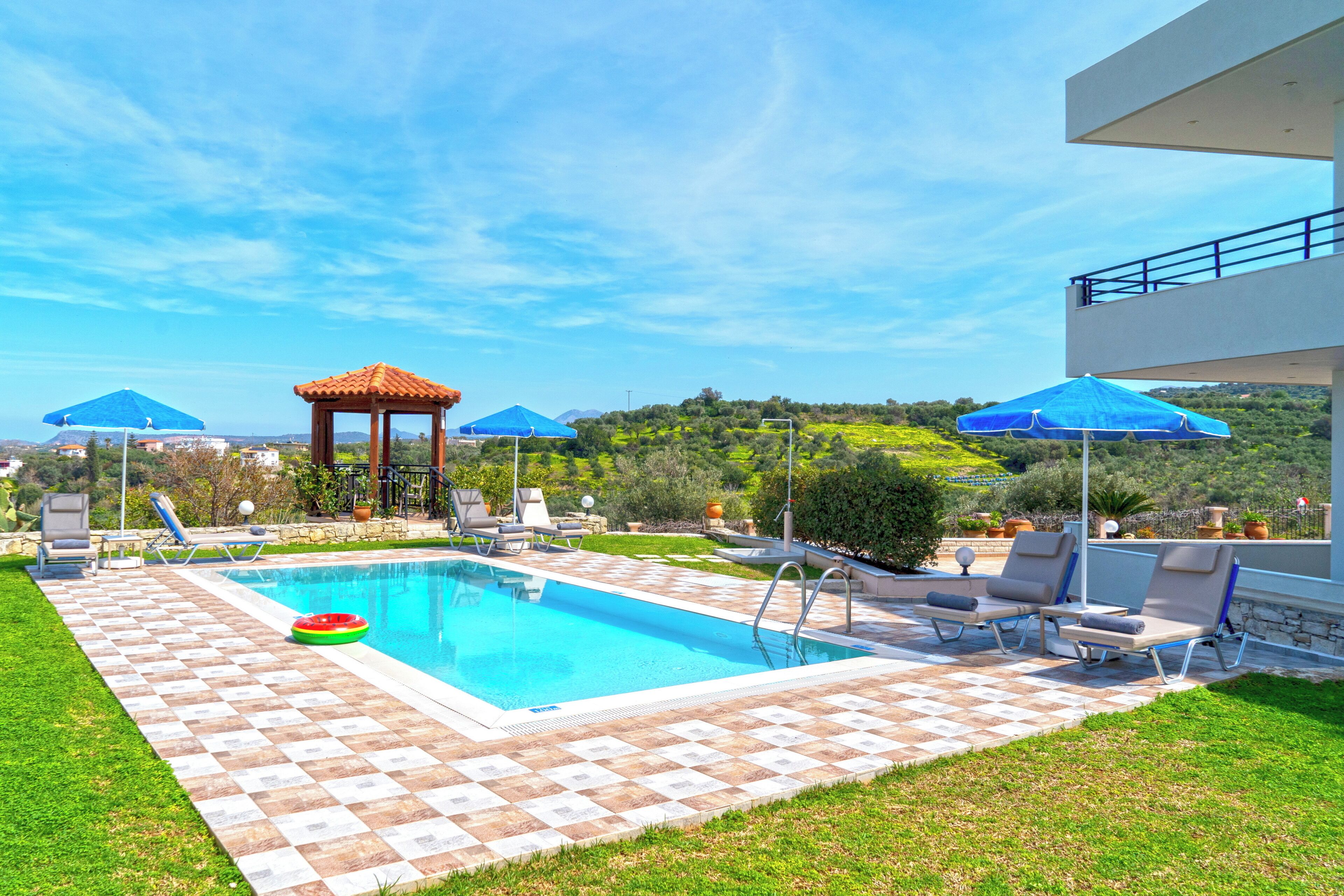 A swimming pool with lounge chairs, a gazebo, and umbrellas.