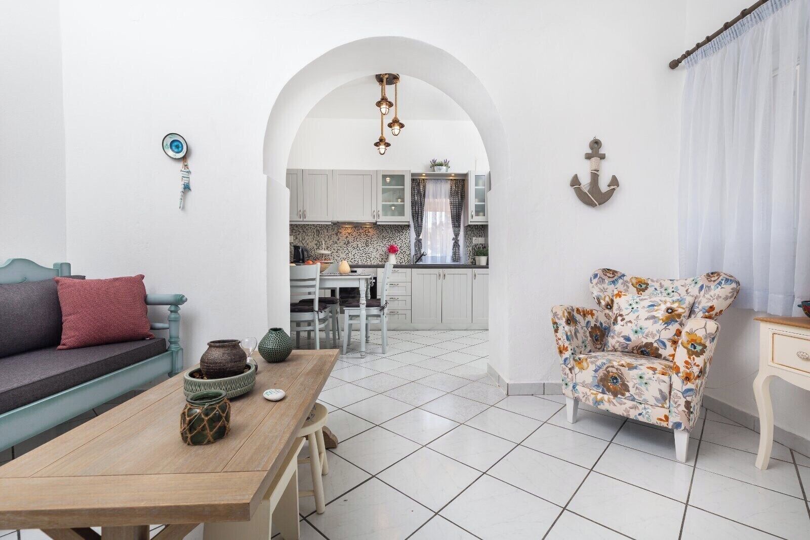Een moderne woonkamer met een bank, een bloemen fauteuil, een houten bijzettafeltje en een keuken op de achtergrond.