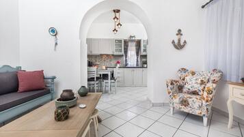 Een moderne woonkamer met een bank, een bloemen fauteuil, een houten bijzettafeltje en een keuken op de achtergrond.