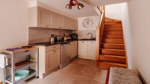 A compact kitchen with a wooden staircase, a clock, and basic appliances. - Ellenboro House, Cosy Sleeps 2, Near Cartmel (Newton-in-Cartmel)