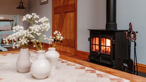 A cozy room with a wood-burning stove, a wooden door, and a table with vases of flowers. - Ellenboro House, Cosy Sleeps 2, Near Cartmel (Newton-in-Cartmel)