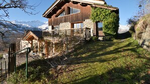Eine Holzhütte mit Steinunterbau, großen Fenstern und einem Balkon mit Holzgeländer.