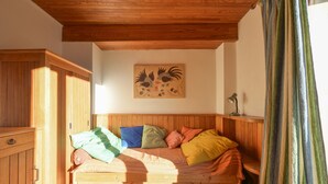 Ein hölzernes Bett mit bunten Kissen, ein Holzschrank und ein an der Wand befestigtes Kunstwerk.