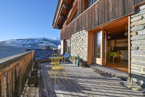 Une terrasse en bois avec une table et des chaises, un mur en pierre et une vue sur une montagne enneigée.