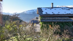 Eine traditionelle Chalet mit Steindeckung, umgeben von schneebedeckten Bergen und üppiger Vegetation.