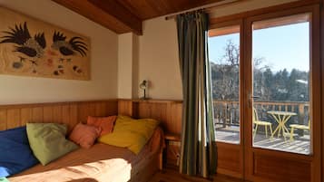 Une pièce de cabane en bois comprenant un lit, une lampe fixée au mur, une fenêtre avec des rideaux et une vue sur une terrasse avec des chaises.