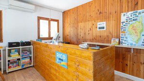 A reception desk with a sign reading 'RICO PLAGE,' a wooden wall, a map on the right, and a window with blinds. - Apartment 'Rico Plage 4 Personnes' with Private Terrace, Wi-Fi and Air Conditioning (Talasani)