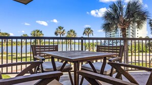 A wooden table and chairs on a balcony with a view of a body of water and palm trees. - Seashell Retreat- Beachfront condo/pools/cabanas (Galveston)