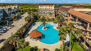 A resort with a central swimming pool, multiple buildings, and a parking area. - Seashell Retreat- Beachfront condo/pools/cabanas (Galveston)
